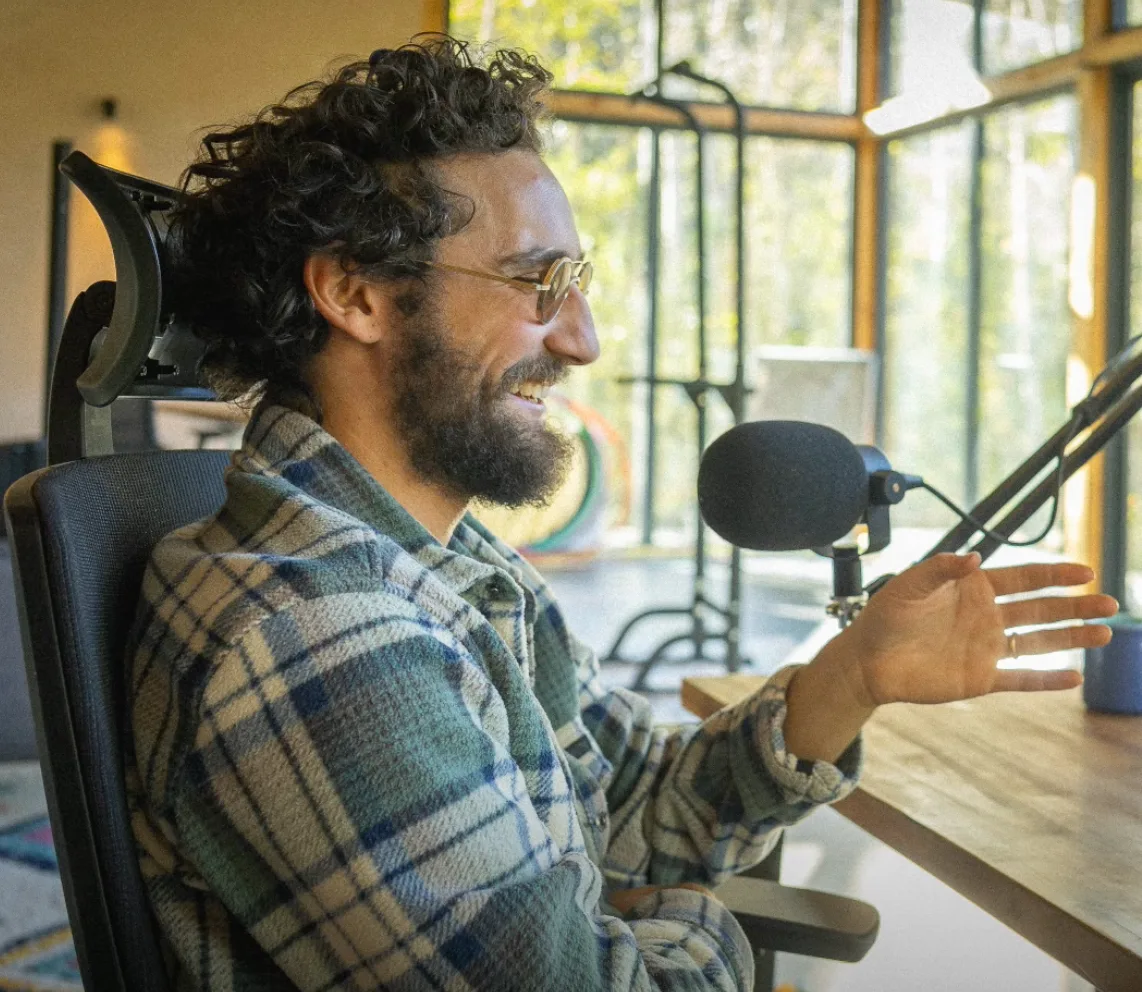 Charly à son bureau, devant un microphone et une fenêtre ouverte sur les arbres