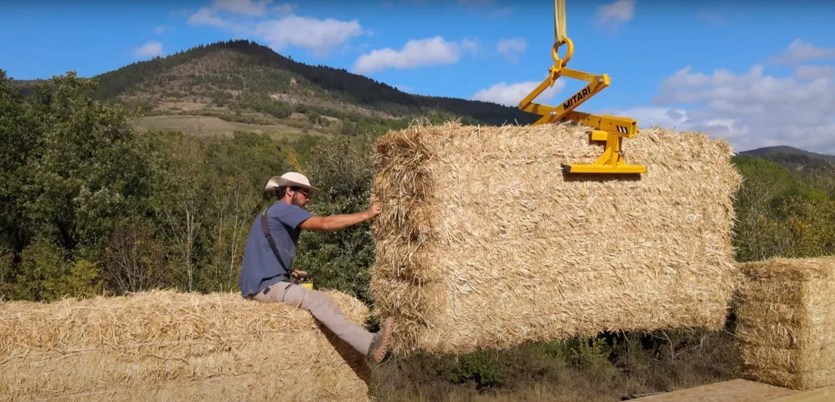 Une personne guide à la main une grosse botte de paille pendant son levage